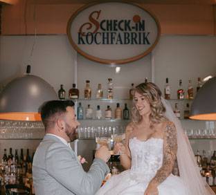 Hochzeitspaar sitzt auf Tresen der Scheck-in Kochfabrik und stößt an